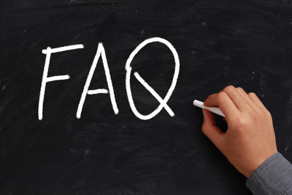 Hand writing "FAQ" on a black chalkboard